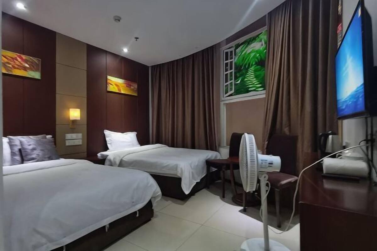 A hotel room with two beds, a desk, a chair, a TV, and a fan.
