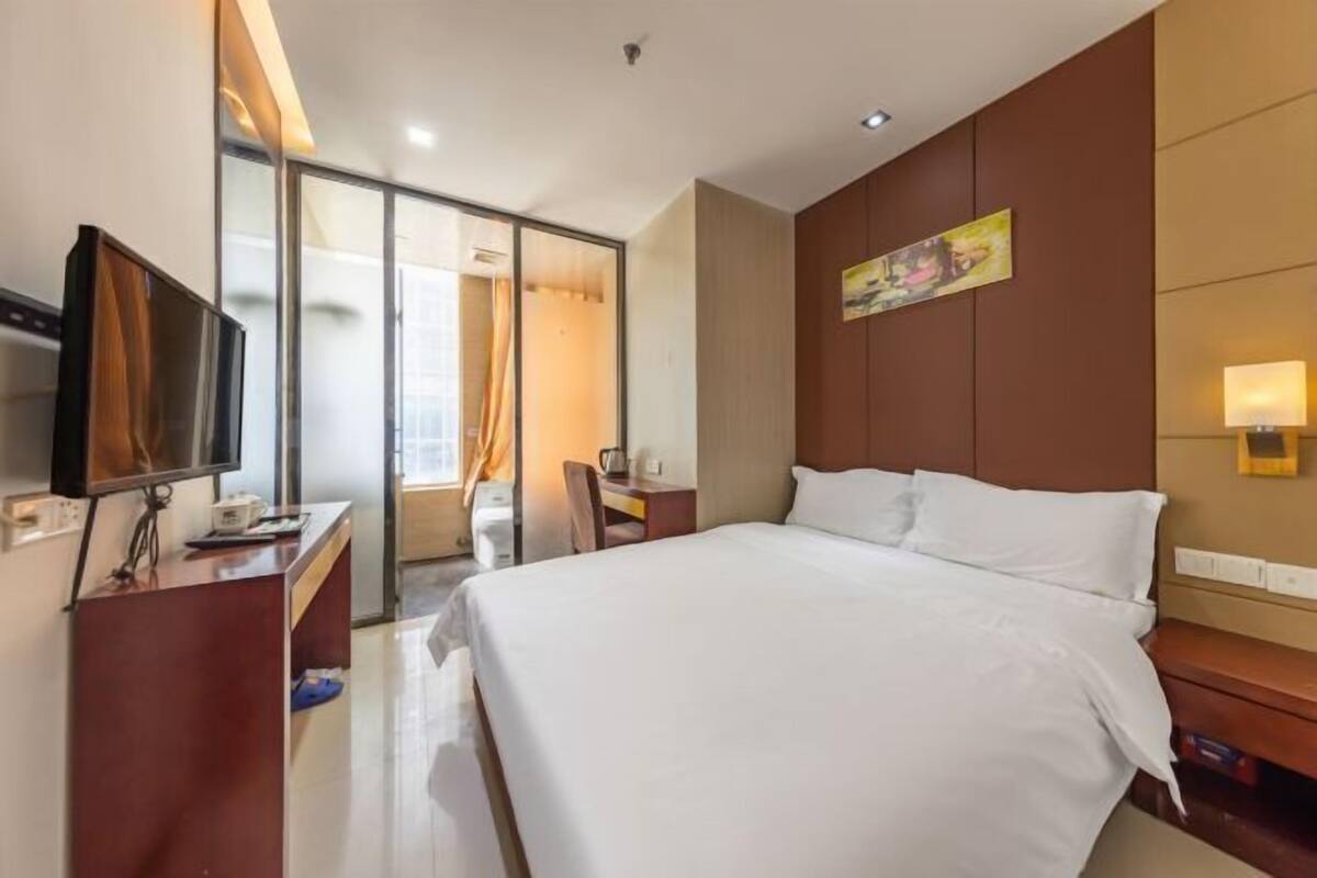 A hotel room with a bed, a desk with a computer, a TV, and a sliding door leading to a bathroom.