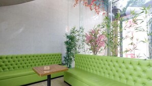 A green sofa and a small table in a room with a glass wall and plants. - Meicheng Hotel (Guangzhou Zhujiang New Town Subway Station) (Guangzhou)