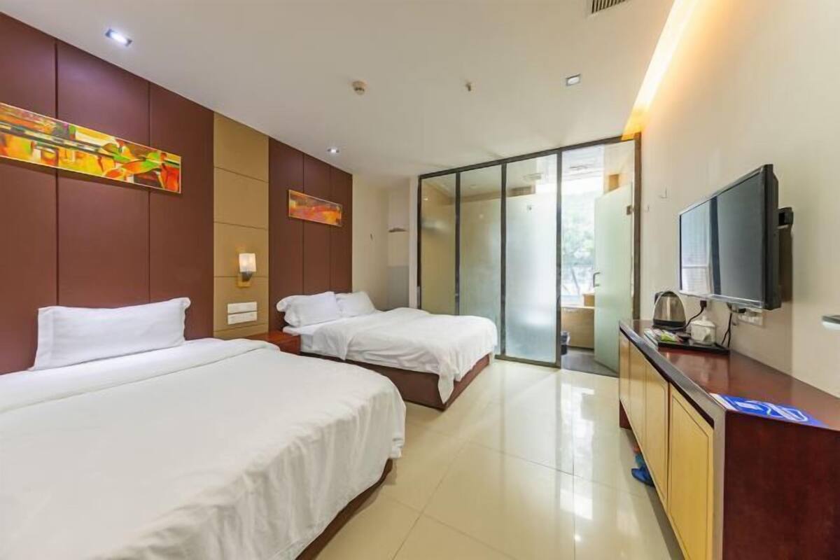 A hotel room with two beds, a TV, a desk, and a sliding door leading to a balcony.