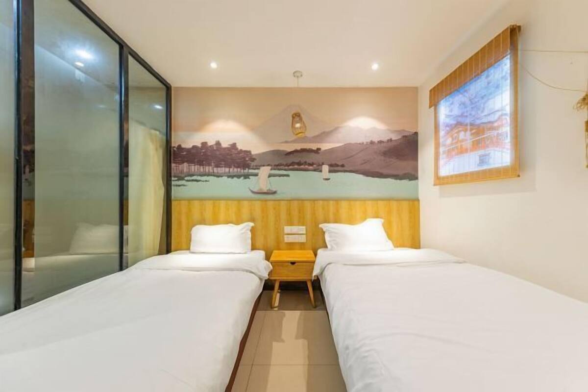 A hotel room with two single beds, a mural on the wall, a window with a view, and a sliding glass door.