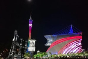 A nighttime cityscape with illuminated buildings, including a prominent tower and a modern structure with a unique roof design. - Meicheng Hotel (Guangzhou Zhujiang New Town Subway Station) (Guangzhou)
