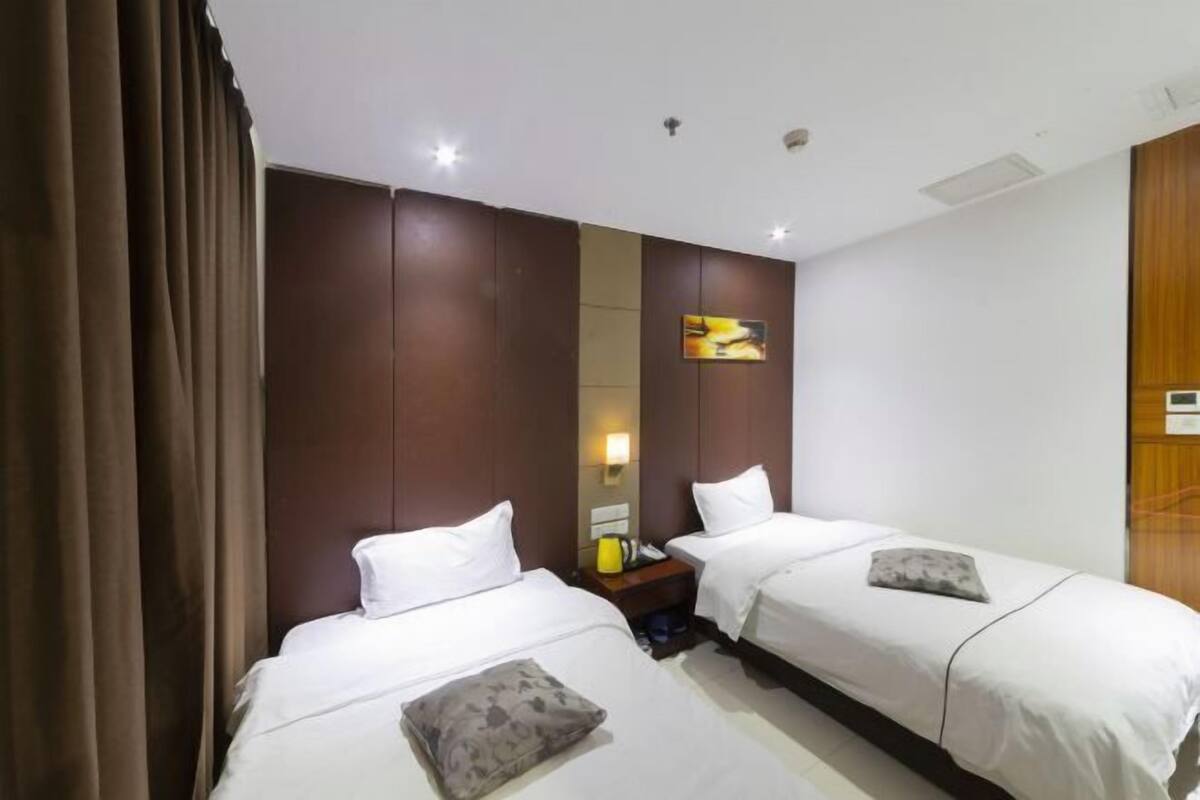 A hotel room with two beds, a nightstand, a lamp, and a painting on the wall.