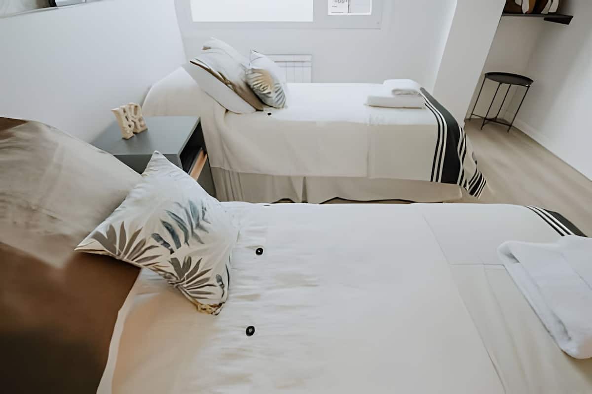 Une chambre à coucher moderne et minimaliste, avec deux lits, une petite table et une chaise.