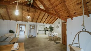 A spacious living area with a high wooden ceiling, a dining table with chairs, a hanging chair, and a sofa.