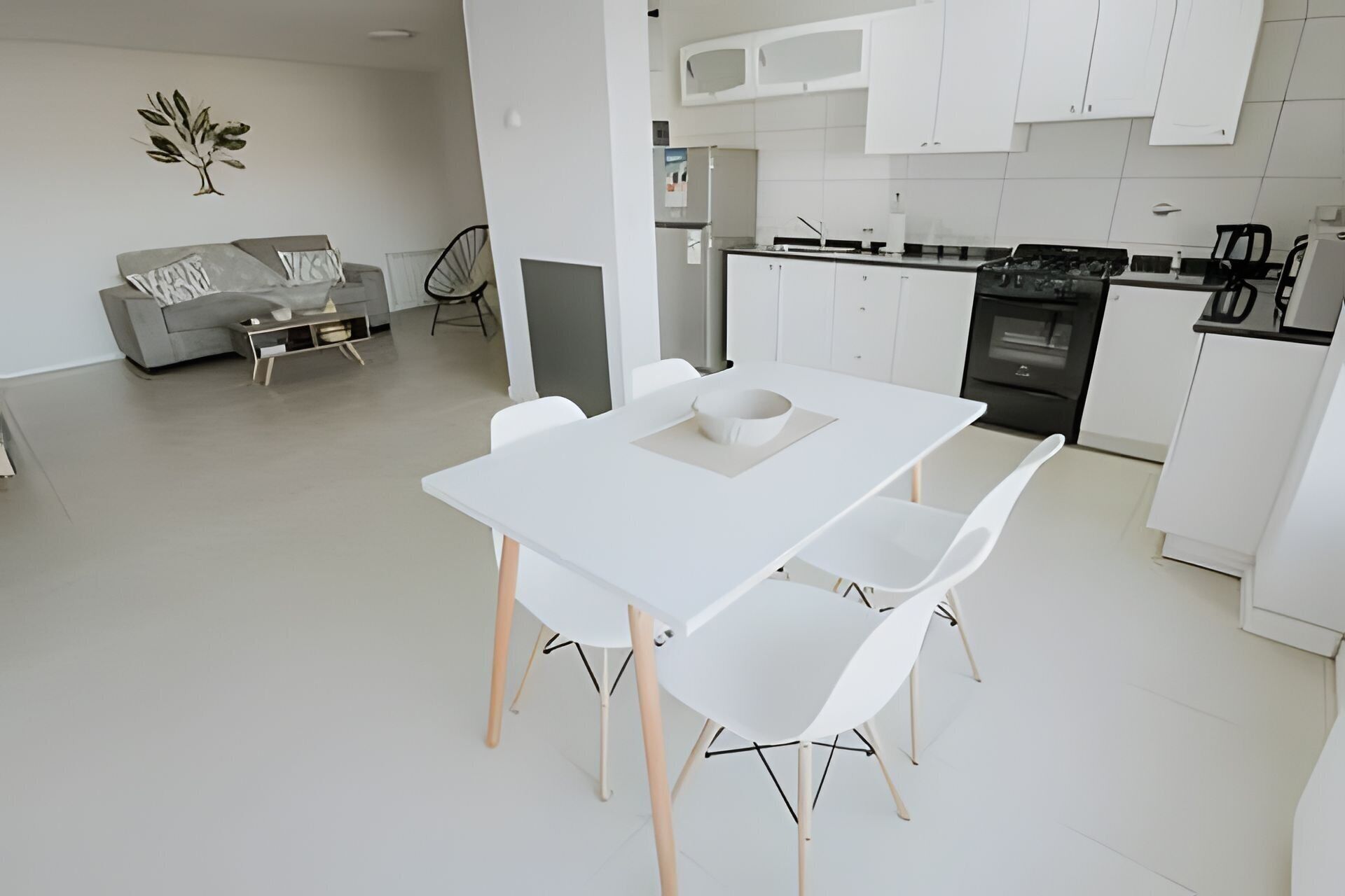 A modern kitchen with white cabinets, a dining table with four chairs, and a sofa in the living area.