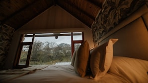 A bedroom with a sloped ceiling, a large window, and a bed with pillows.