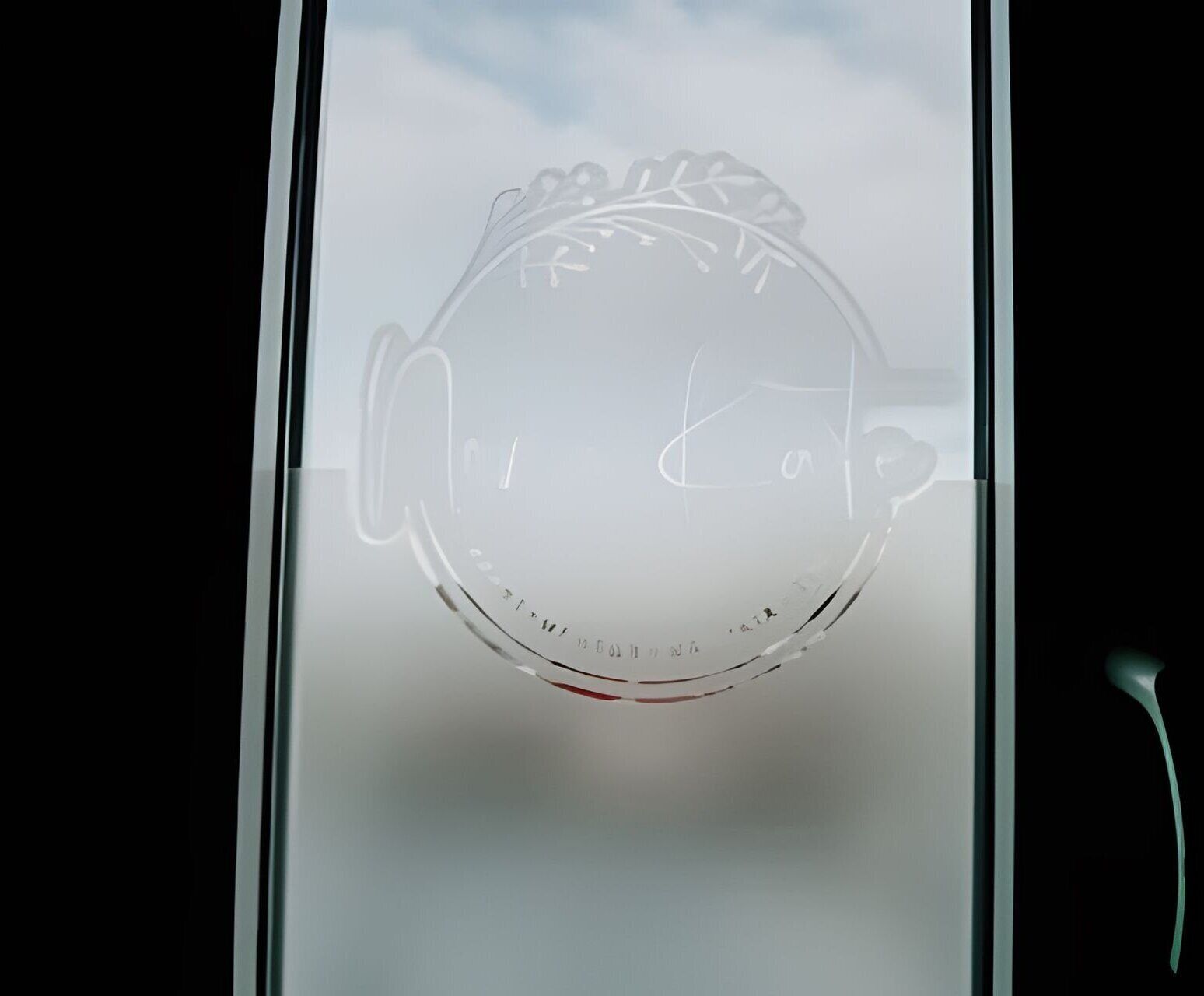 Une fenêtre en verre dépoli ornée d’un motif circulaire, qui pourrait être un logo ou un emblème, et une vue partielle d’une poignée de porte.