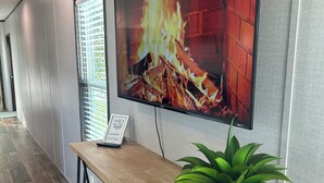 A hallway with a wooden bench, a potted plant, and a TV displaying a fireplace scene. - 8 min to Rocker B - Cozy Lakefront Escape at PK Lake  (Graford)