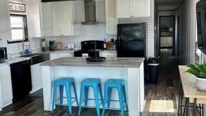 A modern kitchen with white cabinets, a black refrigerator, and a central island with blue bar stools. - 8 min to Rocker B - Cozy Lakefront Escape at PK Lake  (Graford)
