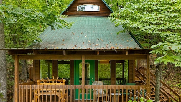 Een houten chalet met een groen dak, een overdekt terras met stoelen en een trap naar de ingang.