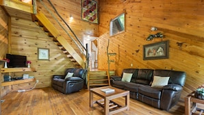 Een gezellig houten cabin interieur met een trap, leren banken, een houten bijzettafeltje en lijstwerken aan de muren.