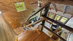Een houten interieur met een trap, een plafondventilator en uitzicht op een tuin door een raam.