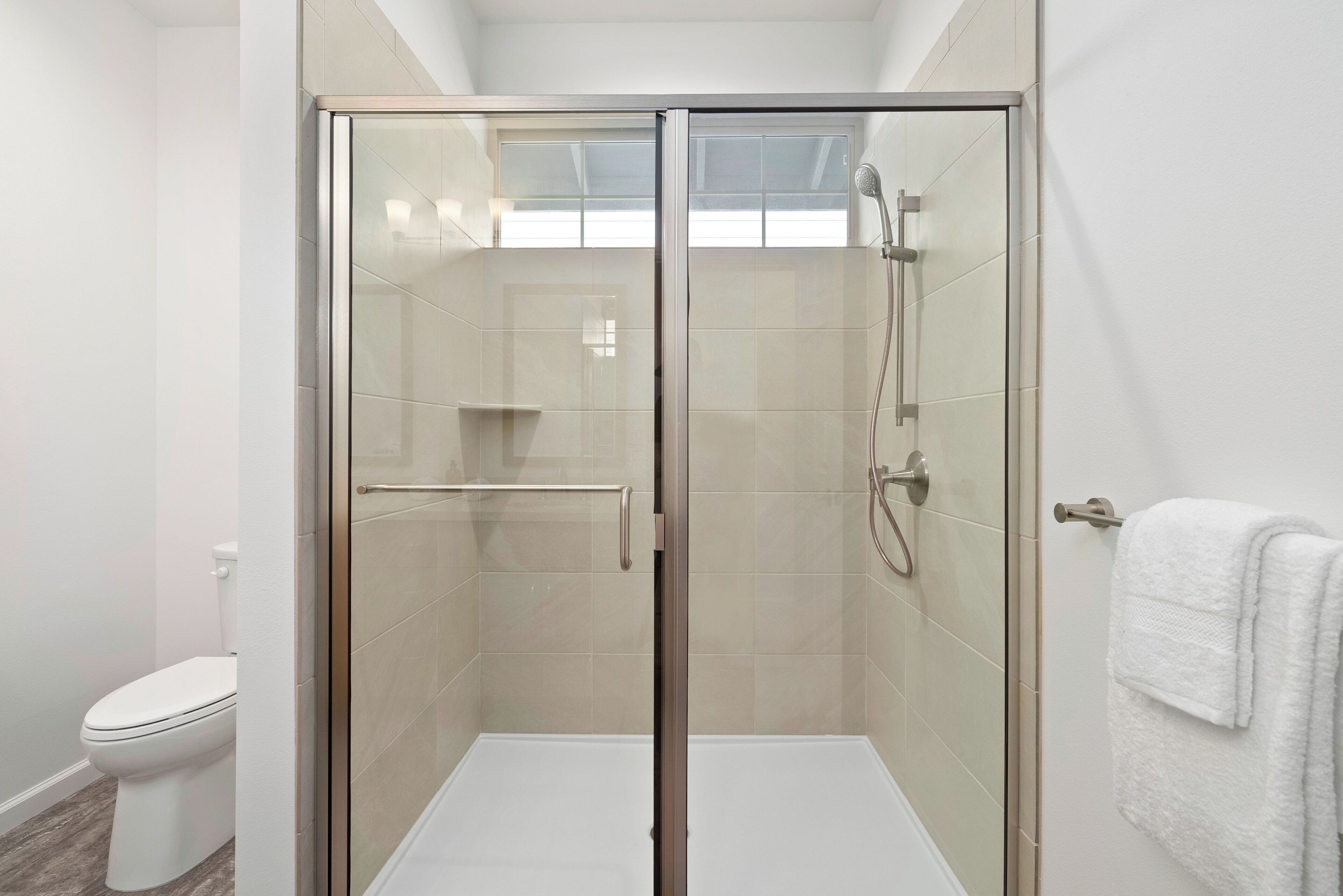 A modern bathroom with a glass-enclosed shower, a toilet, and a towel rack.