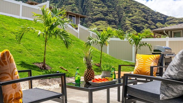 Un patio con mobiliario exterior, una parrilla y vistas a una colina verde y exuberante.