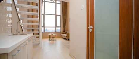 A room with a kitchenette, a window with curtains, a sofa, and a door.
