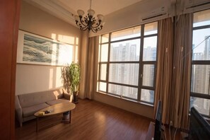 Ein Zimmer mit einer Couch, einem Couchtisch, einer Zimmerpflanze und einem großen Fenster mit Vorhängen.