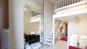 Un appartement moderne comprenant un salon, un téléviseur, un canapé rouge, une table basse blanche, un escalier et un coin cuisine.