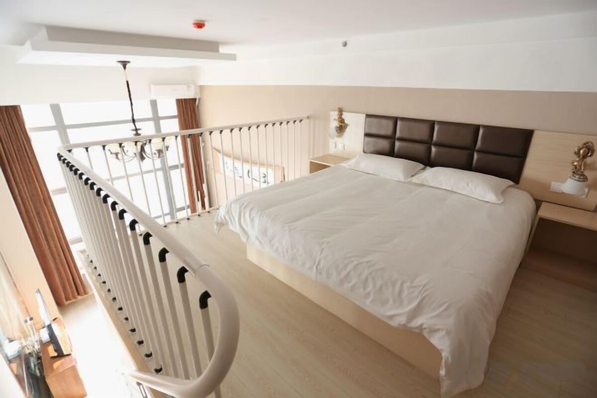 Habitación de hotel con una cama grande, una mesita de noche, una lámpara y vistas al exterior.