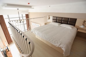 Habitación de hotel con una cama grande, una mesita de noche, una lámpara y vistas al exterior.