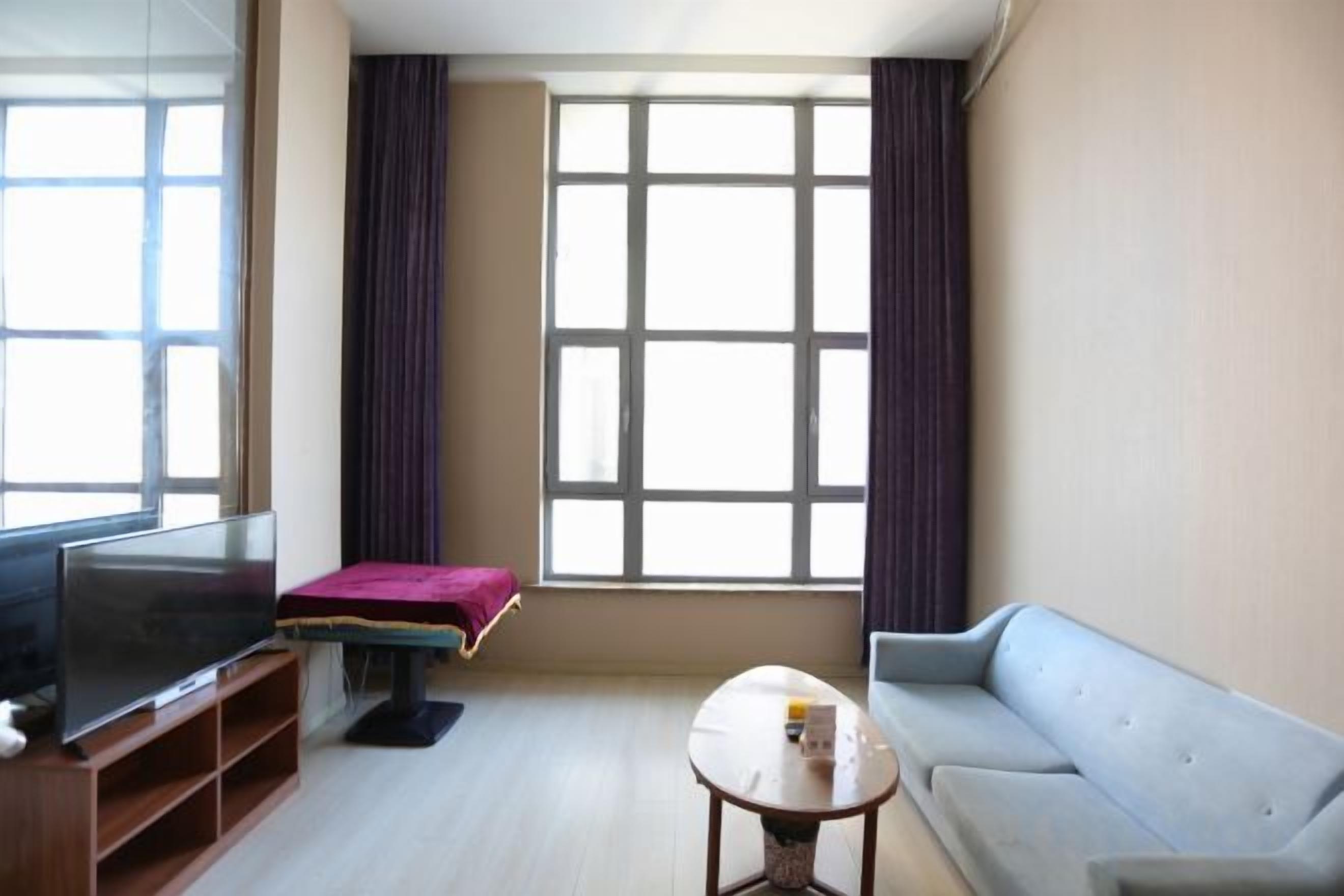 Una sala de estar con televisor, sofá, mesa de centro y una ventana con cortinas.