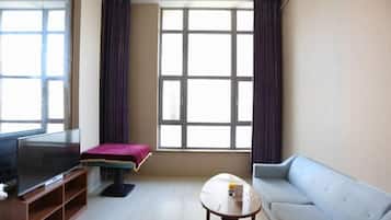 Una sala de estar con televisor, sofá, mesa de centro y una ventana con cortinas.