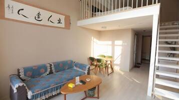 A room with a sofa, a small table, a balcony, and a staircase.