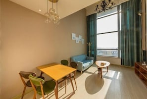 A modern living room with a dining table, chairs, a sofa, a round coffee table, and a large window with curtains.