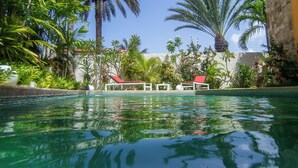 A swimming pool with clear blue water, surrounded by palm trees and a building with a stone facade. - Posada Libert Hotel (Díaz)
