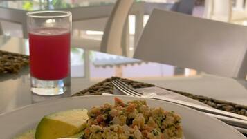 A breakfast plate with scrambled eggs, avocado slices, cheese, and arepas, with a glass of red juice on the table.
