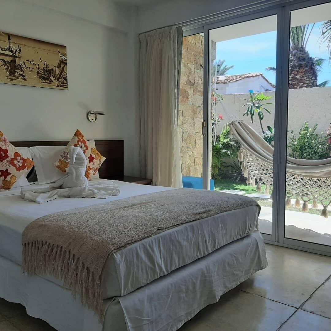 Una camera d'albergo con un letto, un'ampia finestra e un'amaca all'esterno.