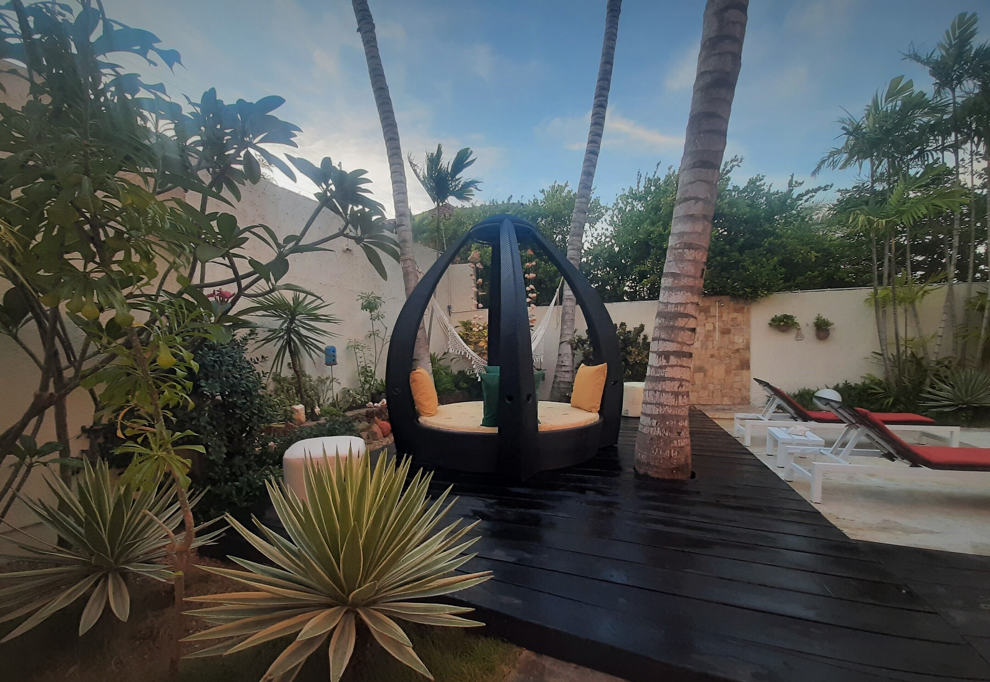 A circular swing chair with a cushioned seat and backrest, surrounded by palm trees and potted plants.