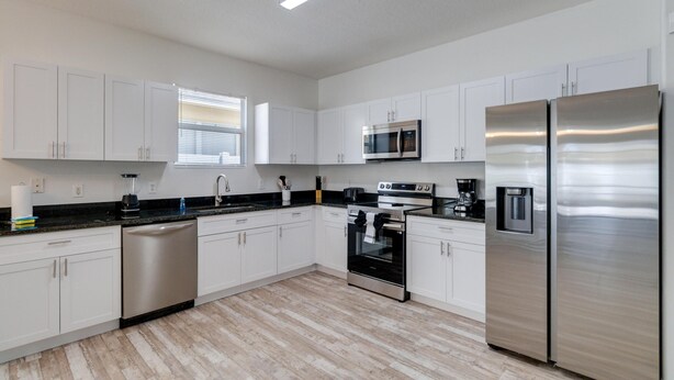 A modern kitchen with white cabinets, stainless steel appliances, and a black countertop.