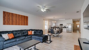 A modern living room with a sectional sofa, a dining area, and a kitchen in the background.
