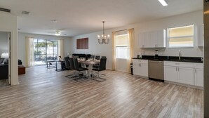 A modern kitchen with white cabinets, a dining area with a table and chairs, and a large window with blinds.