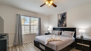 A bedroom with a bed, nightstands, a ceiling fan, a window with curtains, and a painting on the wall.