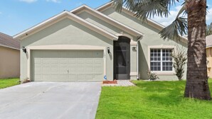 A single-story house with a garage, a front door, and a palm tree in the yard.