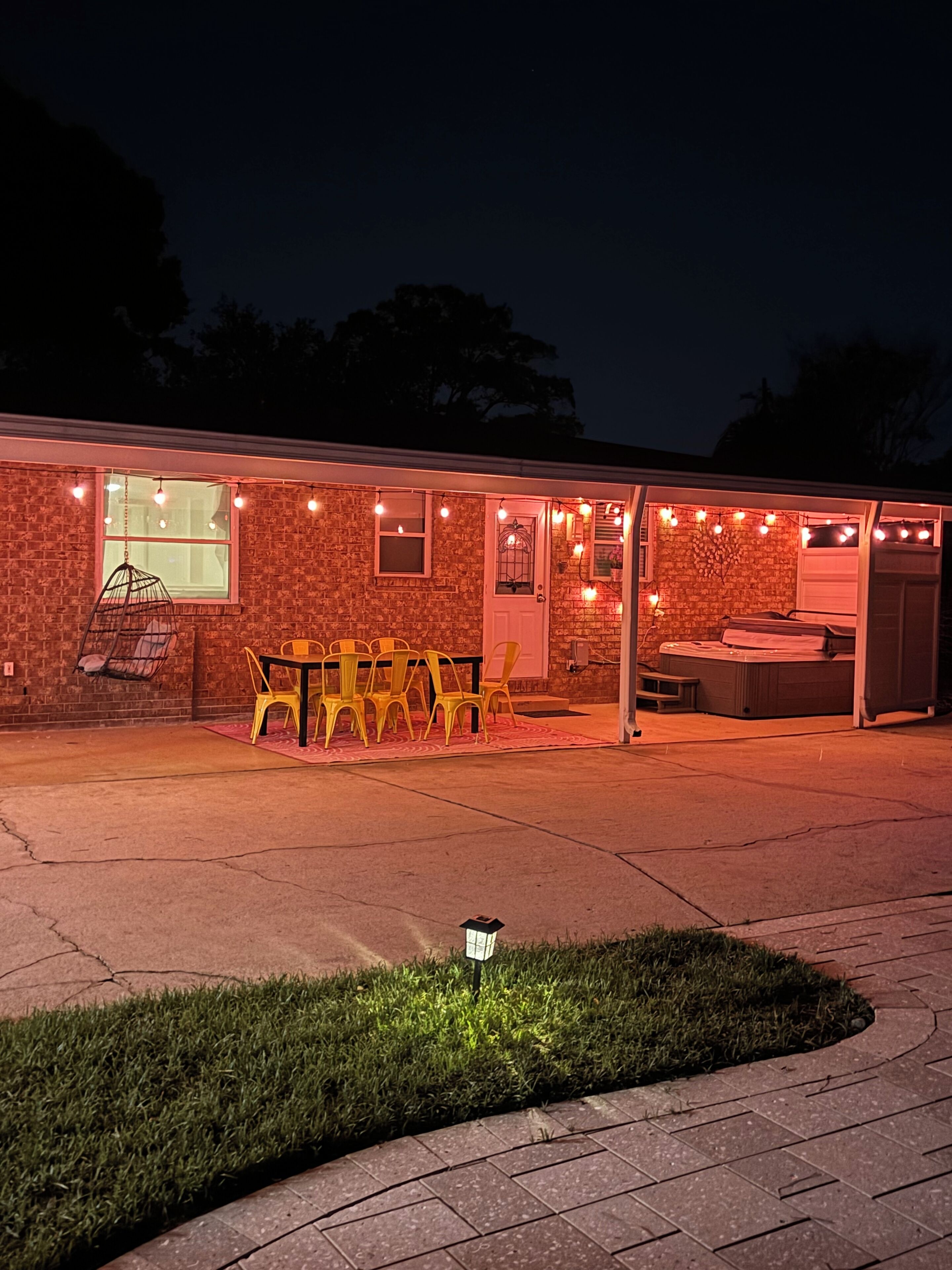 A brick building with a patio area featuring a table and chairs, a hanging chair, and string lights.