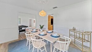 A dining area with a wooden table set for four, white chairs, a gold serving cart, and a hanging pendant light. - Relaxing SWEET HOME 9mi Downtown Pool&Hot tub. (Jacksonville)