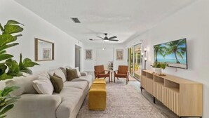 A modern living room with a sofa, ottoman, and chairs, a TV mounted on the wall, and a large window with a view. - Relaxing SWEET HOME 9mi Downtown Pool&Hot tub. (Jacksonville)