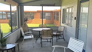 A covered patio area with a table and chairs, a ceiling fan, and a view of a wooden building in the background. - Relaxing Lake Retreat (Lake Placid)