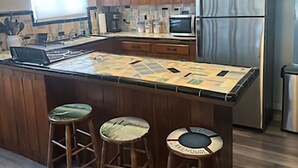 A kitchen with wooden cabinets, a stainless steel refrigerator, a microwave, and a large island with stools. - Relaxing Lake Retreat (Lake Placid)