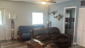 A living room with a brown leather sofa, a blue couch, a ceiling fan, and a window. - Relaxing Lake Retreat (Lake Placid)