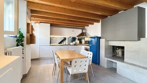 Una cocina moderna con vigas de madera, una mesa de comedor con sillas, un refrigerador azul y una chimenea.