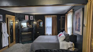 Une chambre d’hôtel avec un lit, une coiffeuse avec un miroir, une cheminée et une fenêtre avec des rideaux.