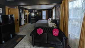 Une chambre d’hôtel avec un canapé noir, un lit, une télévision, une cheminée et une grande fenêtre avec des rideaux.