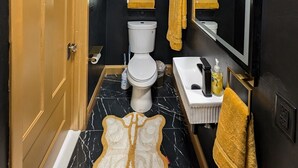 Une salle de bain équipée de toilettes, d’un lavabo et d’un miroir. On y trouve des serviettes et des articles de toilette sur le comptoir du lavabo.
