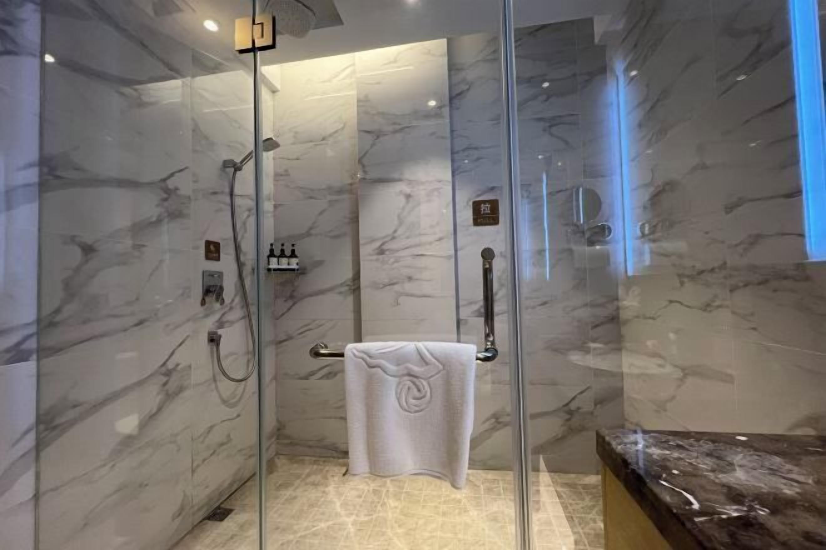 Une douche fermée par des parois de verre, avec des murs en marbre, un porte-serviettes et un plan de travail en marbre.