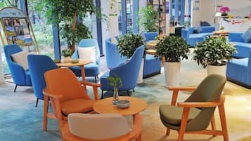 Un espace de détente moderne, doté de sièges et de tables, et agrémenté de grandes fenêtres et de plantes d’intérieur.
