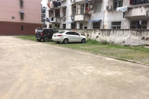 A parking area with two cars, a concrete surface, and a building with multiple balconies and laundry hanging.